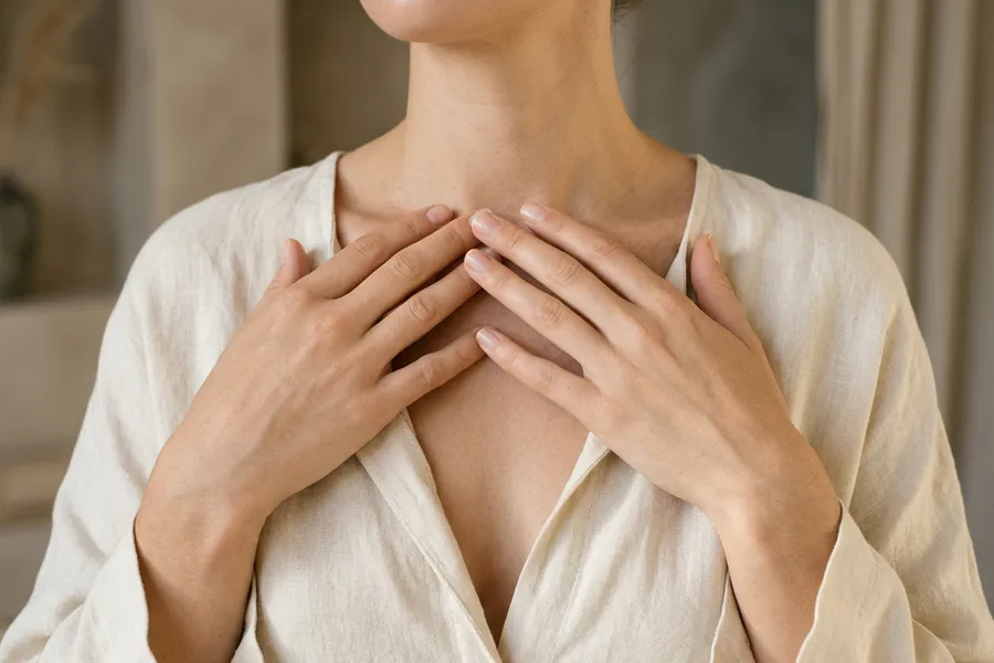 A woman's hands resting at her collarbone in a linen top