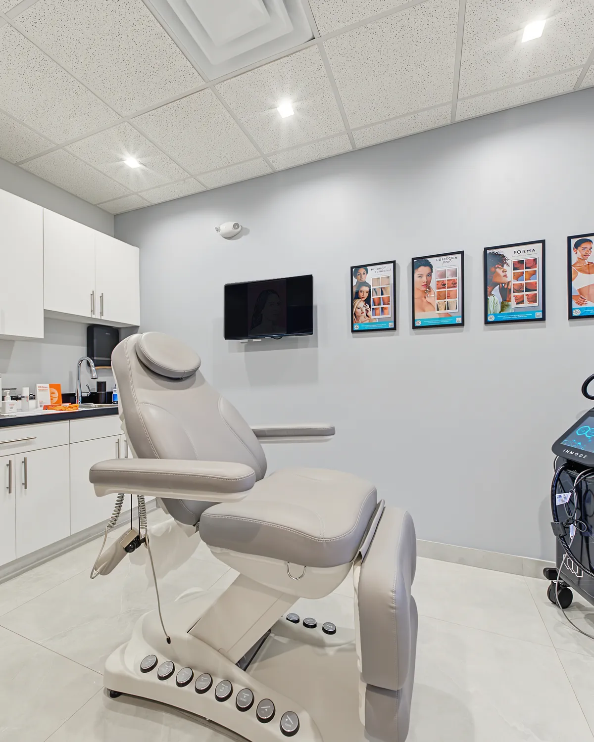 A bright treatment room at AWE with a reclining treatment chair and before and after prints on the wall